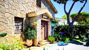 Un bâtiment en pierre avec une entrée carrelée, des plantes en pot et un grand arbre.