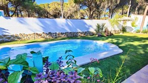 Une piscine entourée d’un mur de pierre, avec une pelouse et des arbres en arrière-plan.