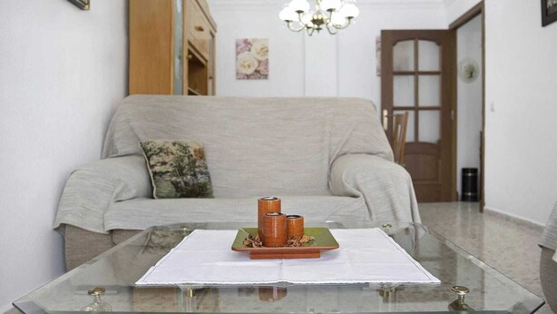 A living room with a glass coffee table, a sofa, a chandelier, and a door in the background. - Centrally located apartment in Conil Pepa's House (Conil)