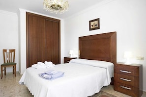A hotel room with a large wooden wardrobe, a bed with white linens, a chair, and a bedside table with a lamp. - Centrally located apartment in Conil Pepa's House (Conil)