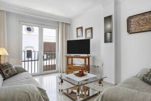 A living room with a flat-screen TV on a wooden stand, a glass coffee table, and two sofas.