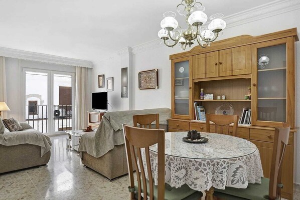 A living room with a dining table, chairs, a sofa, a TV, and a wooden cabinet with glass doors.