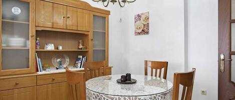 A dining area with a round table, chairs, a lace tablecloth, wooden cabinets, and a chandelier.