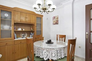 A dining area with a round table, chairs, a lace tablecloth, wooden cabinets, and a chandelier.