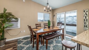 A dining area with a wooden table, chairs, a bench, a chandelier, a potted plant, and a view of a snowy landscape through large windows. - Spacious home on a vineyard near Gorge Amp.,Leavenworth,chelan and Mission Ridge (East Wenatchee)