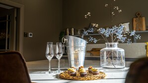 Une table à manger avec un seau en métal, un vase en verre contenant des fleurs et une planche à découper en bois.