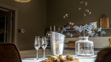 A dining table with a metal bucket, a glass vase with flowers, and a wooden cutting board.