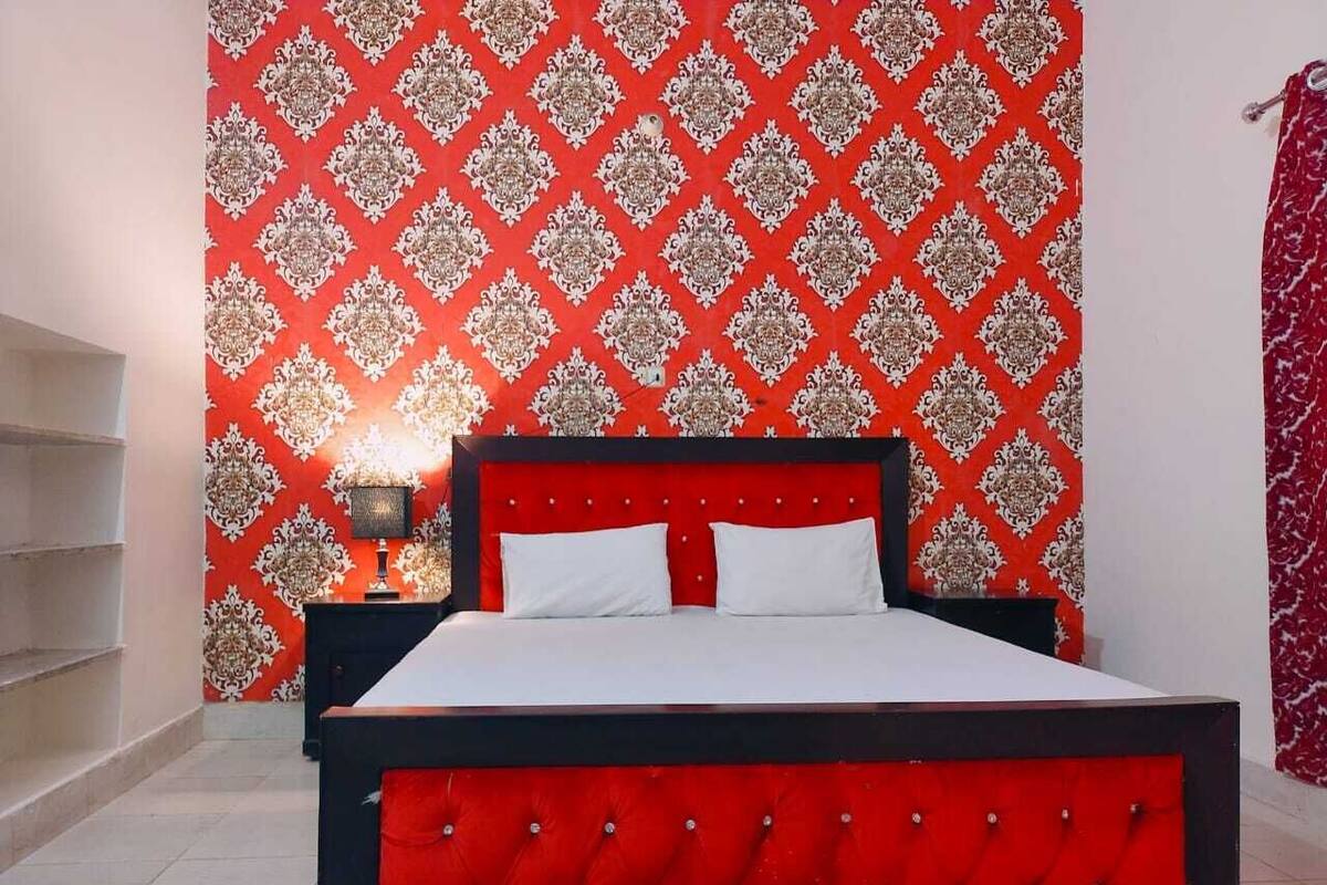 Una cama con estructura roja y ropa de cama blanca en una habitación con papel tapiz estampado.