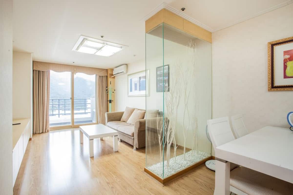 A modern hotel room with a balcony, a glass partition, a sofa, a dining table, and a white chair.