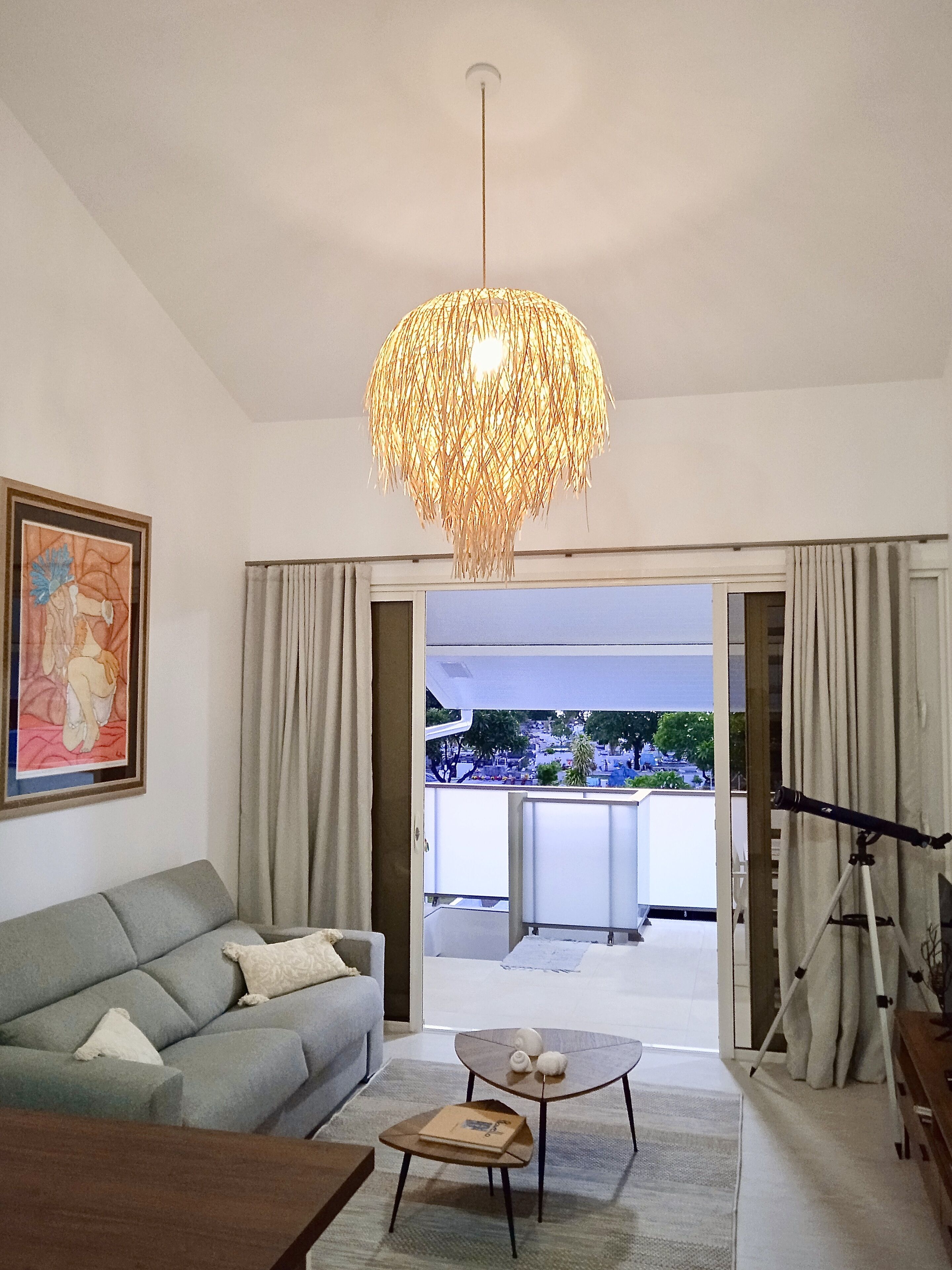 A modern living room with a grey sofa, a coffee table, and a hanging light fixture.