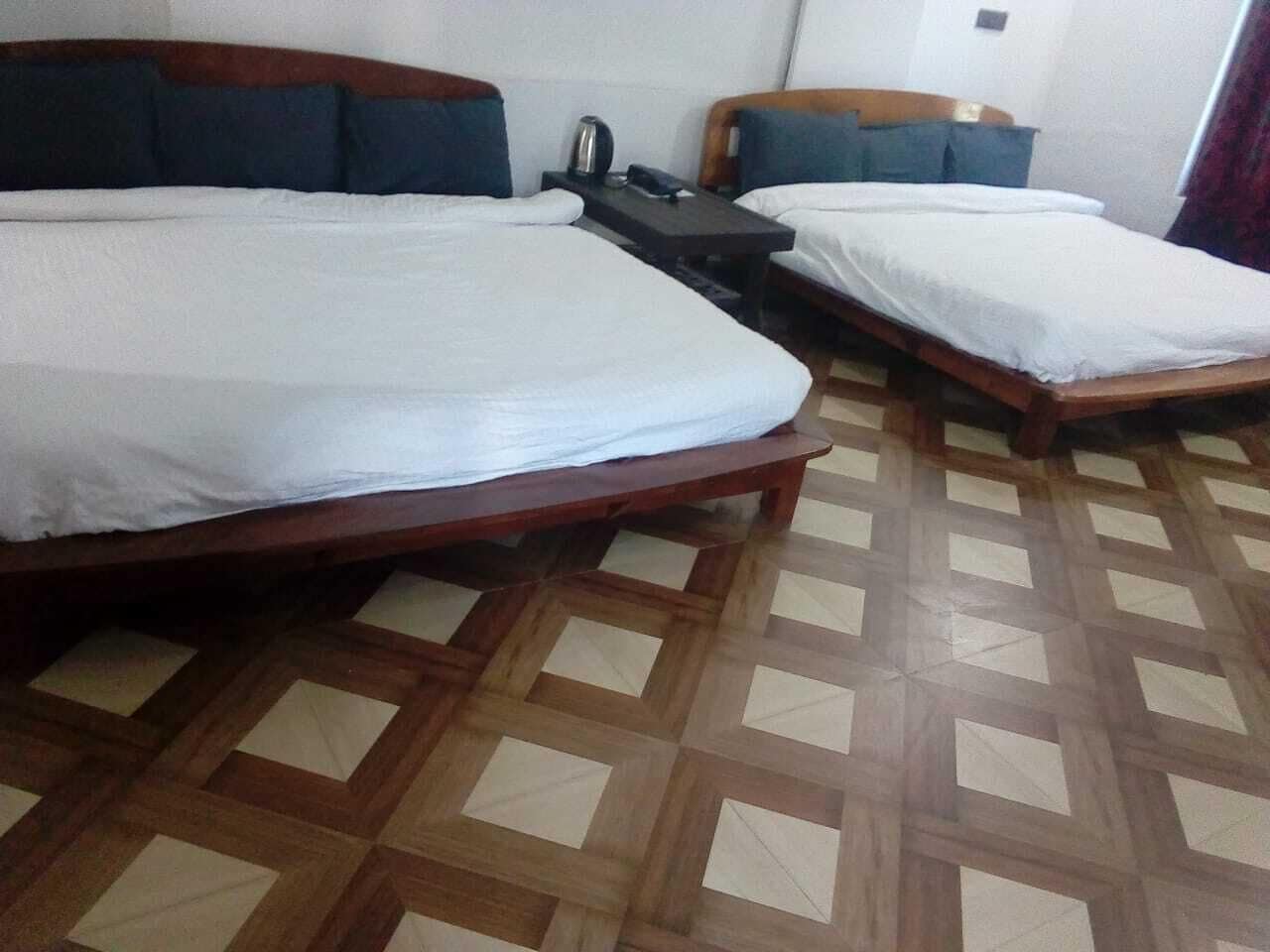 A hotel room with two single beds, a small table with a kettle, and a patterned floor.
