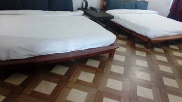 A hotel room with two single beds, a small table with a kettle, and a patterned floor.