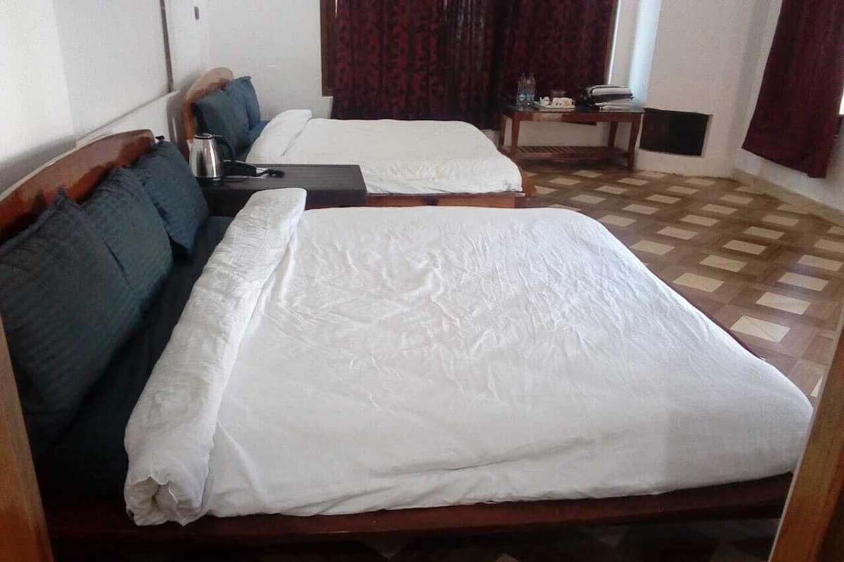 A room with two beds, a small table with a lamp, and a window with curtains.