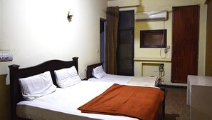 A hotel room with two beds, a wooden headboard, a brown blanket, a wall-mounted air conditioner, and a small window with curtains. - Shamrock Hotel (Lahore)