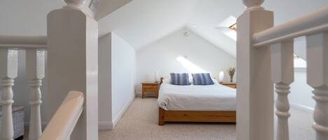Une chambre avec un lit en bois, des murs blancs et un plafond en pente.