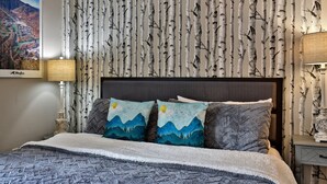A bedroom with a bed, two pillows with mountain designs, a wall-mounted lamp, and a framed picture on the wall. - The Hideaway Retreat at Mountain Green 1 BR/1 BA Condo, Steps to the Mountain, Amenities. (Killington)