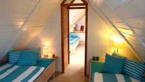 A small, cozy attic bedroom with two beds, a wooden door, and a view into another room.