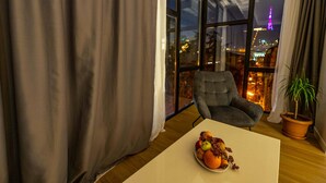A modern living room with a large window, a grey armchair, a table with fruit, and a potted plant. - Address Boutique Hotel (Tbilisi)