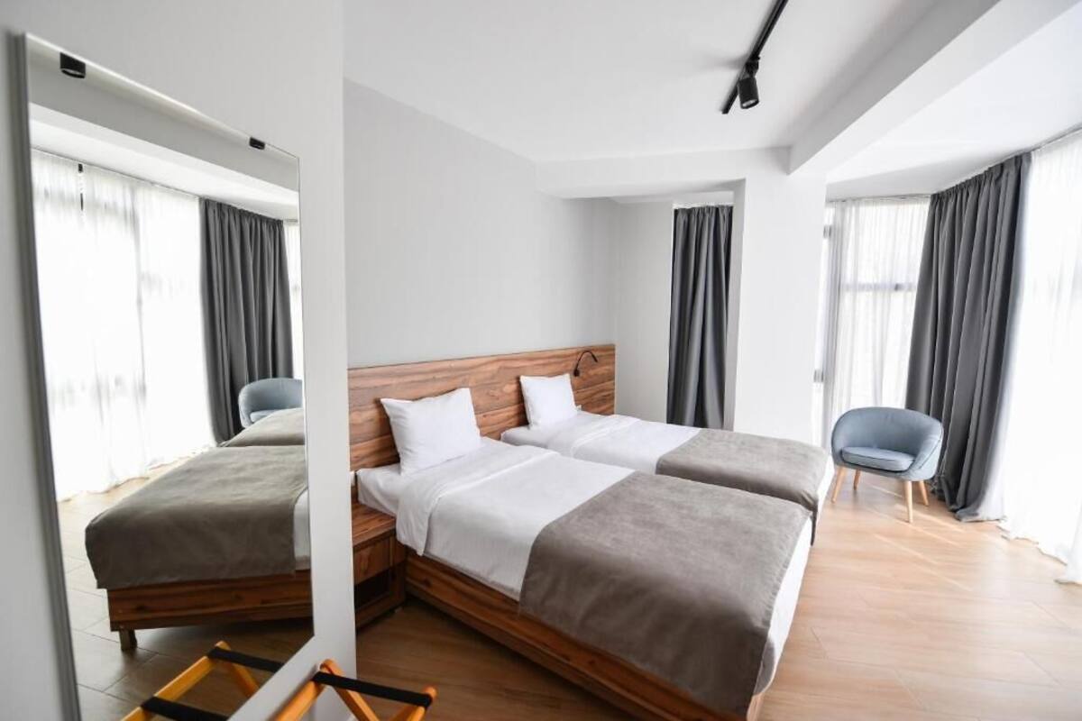A hotel room with two beds, a wooden headboard, a chair, and large windows with curtains.