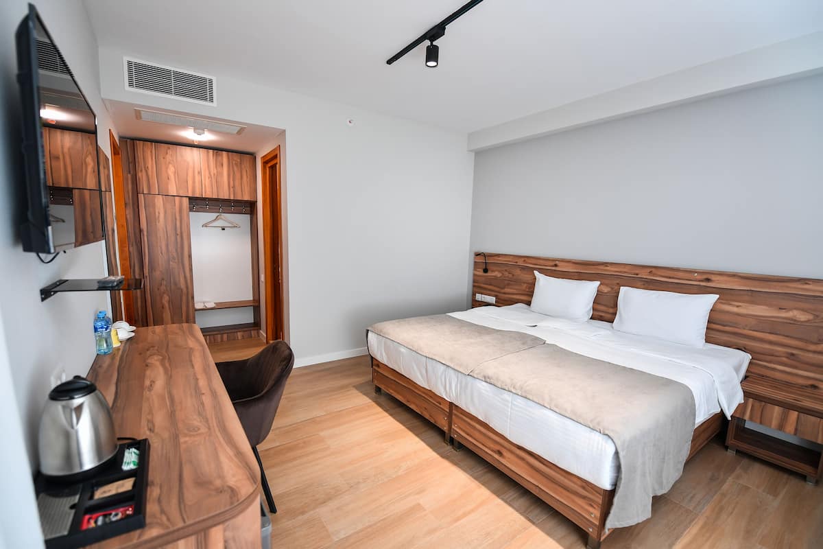A bedroom with a wooden bed, a desk with a kettle, a chair, and a TV mounted on the wall.