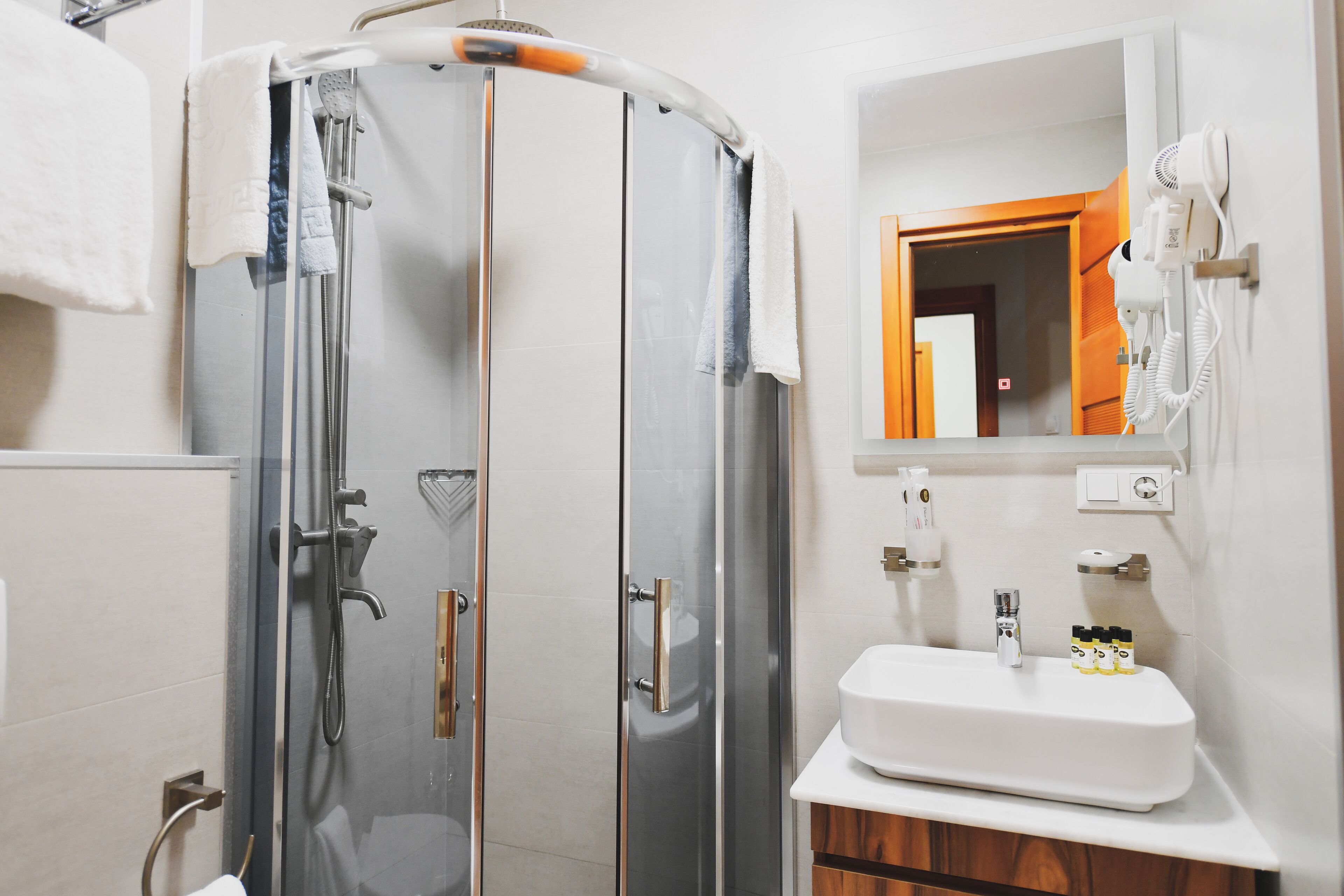 A modern bathroom with a glass-enclosed shower, a white sink, and a hairdryer mounted on the wall.