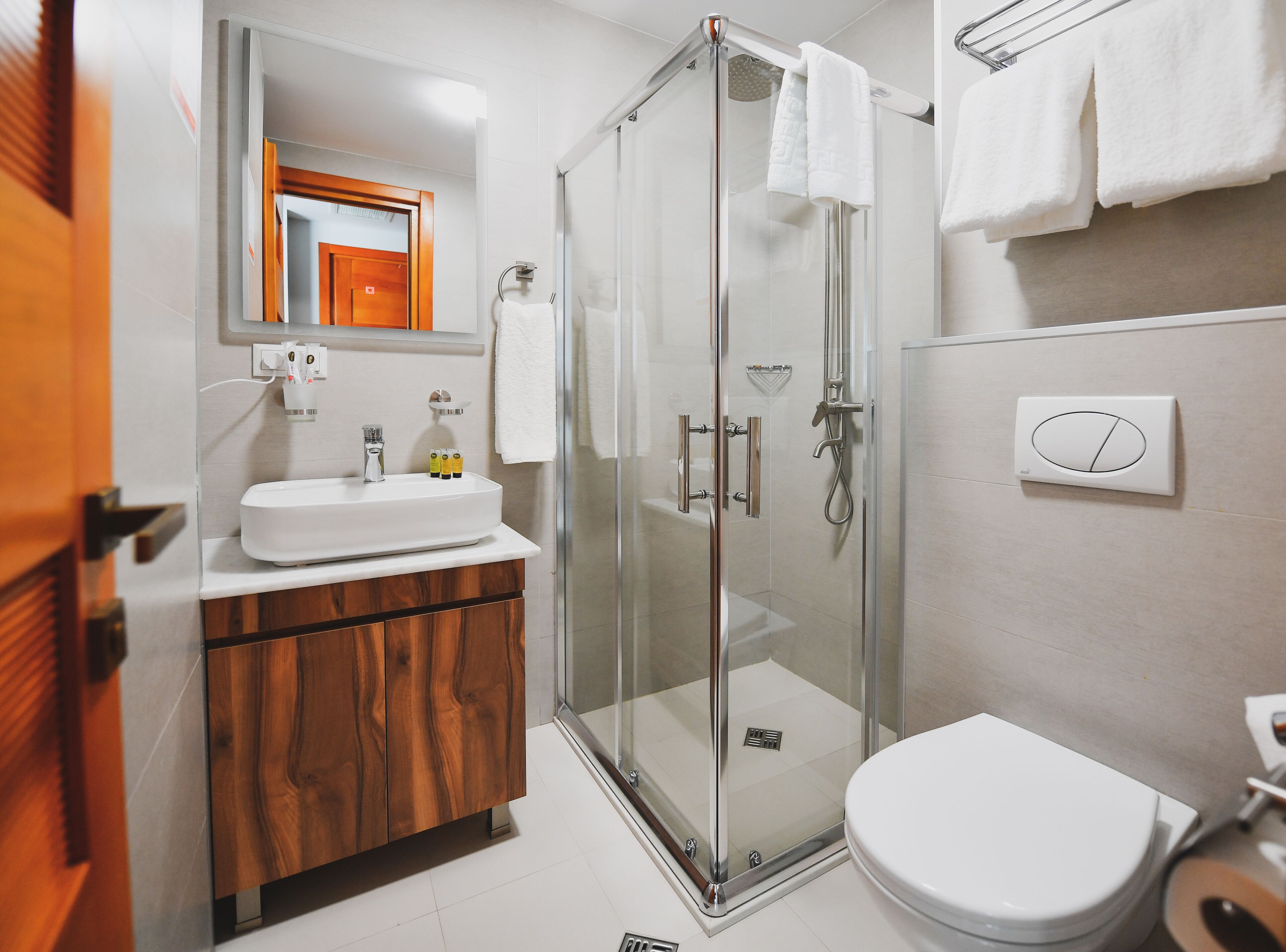 A modern bathroom with a glass-enclosed shower, a wooden vanity, a white sink, and a toilet.