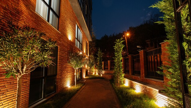 A brick building with a paved walkway, illuminated by ground lights, surrounded by greenery. - Address Boutique Hotel (Tbilisi)