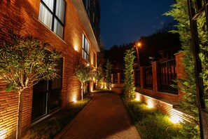 A brick building with a paved walkway, illuminated by ground lights, surrounded by greenery. - Address Boutique Hotel (Tbilisi)
