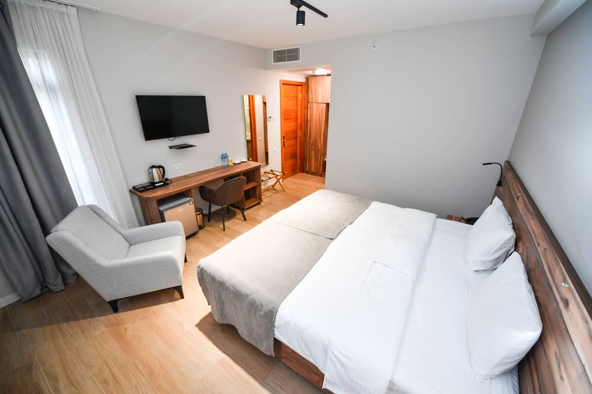 A hotel room with a bed, a desk, a chair, a television, and a wardrobe.