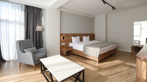 A modern hotel room with a large bed, a grey armchair, a bedside table, and a wooden headboard. - Address Boutique Hotel (Tbilisi)