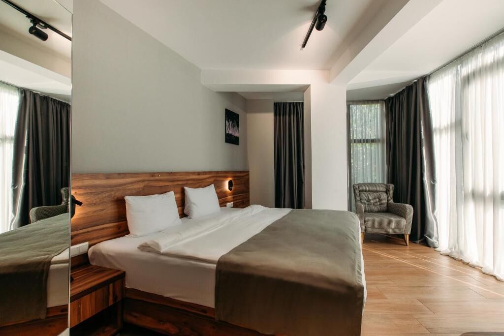 A modern hotel room with a large bed, wooden headboard, and a chair.