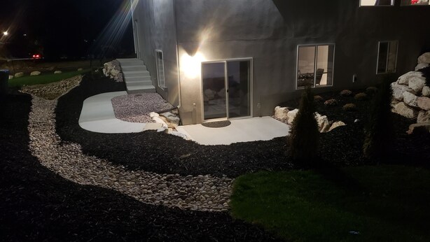 Una casa moderna con fachada de piedra, un acceso bien iluminado y un camino de entrada ajardinado con guijarros y mantillo.