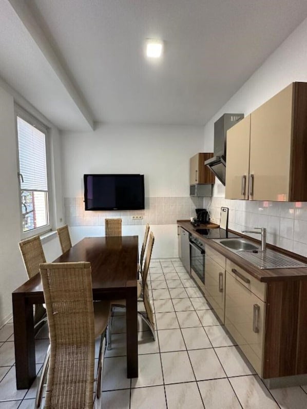 A compact kitchen with a dining table and chairs, a television mounted on the wall, and wooden cabinets.