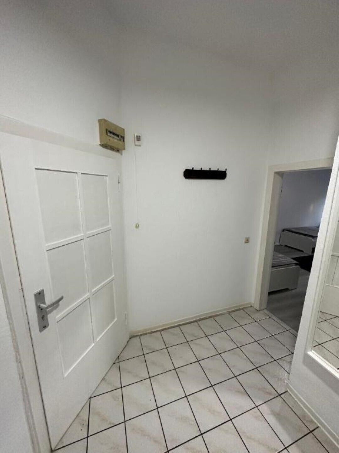 A hallway with a white door, a black coat rack, and a tiled floor.