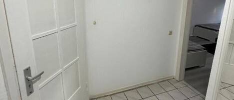 A hallway with a white door, a black coat rack, and a tiled floor.