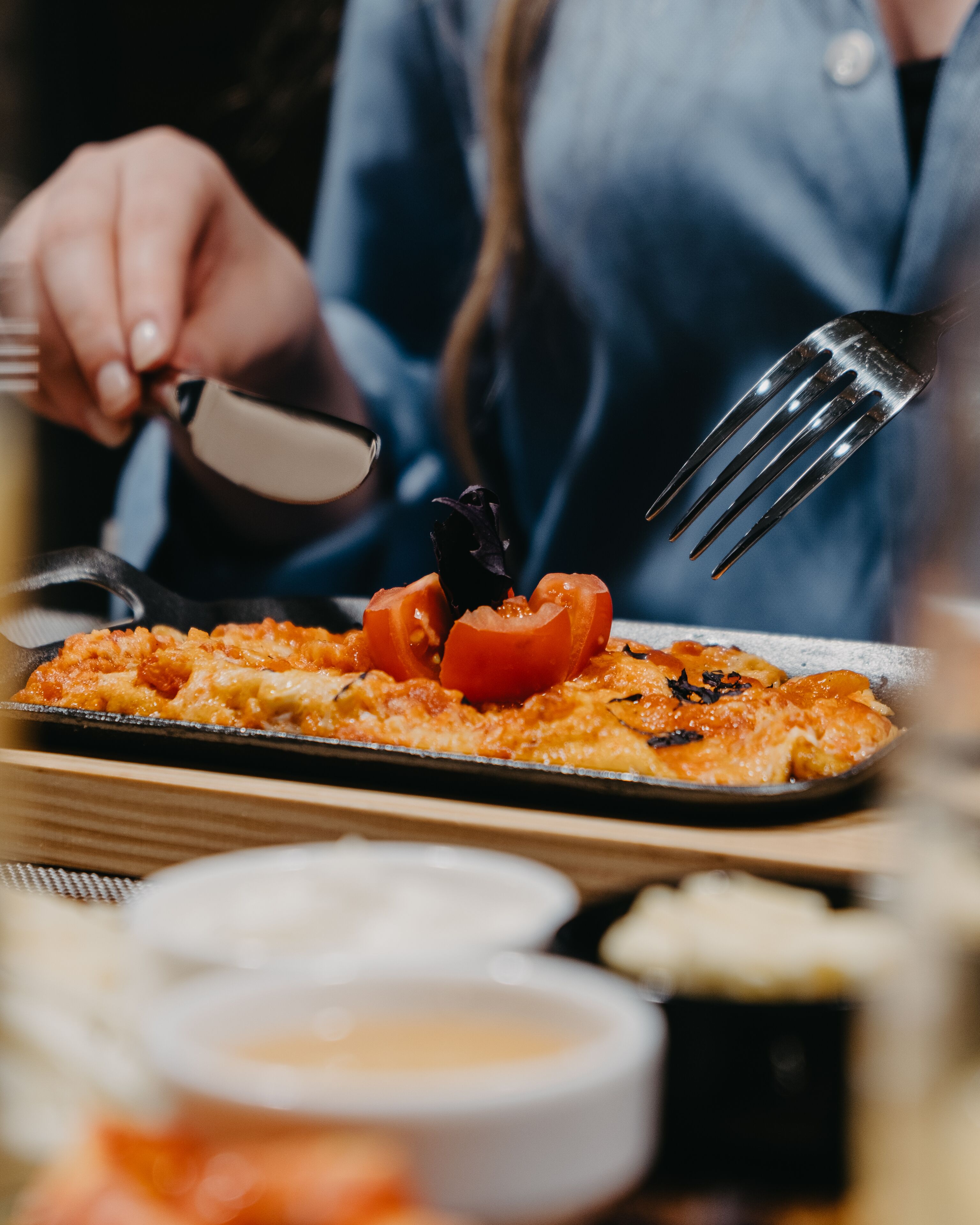 Una mesa de comedor con comida, que incluye una pizza con tomates y queso, un tenedor y un cuchillo.
