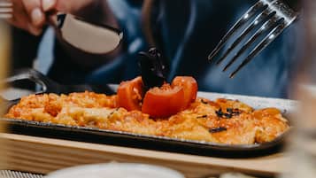 Una mesa de comedor con comida, que incluye una pizza con tomates y queso, un tenedor y un cuchillo.