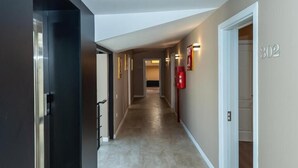 Um corredor com carpete bege, moldura de porta preta e um extintor de incêndio na parede.