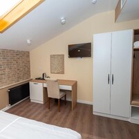 Een slaapkamer met een bed, een bureau, een stoel, een kledingkast, een radiator en een televisie.