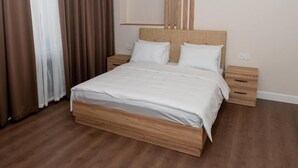 Quarto moderno com estrutura de cama de madeira, roupa de cama branca e mesa de cabeceira com abajur.