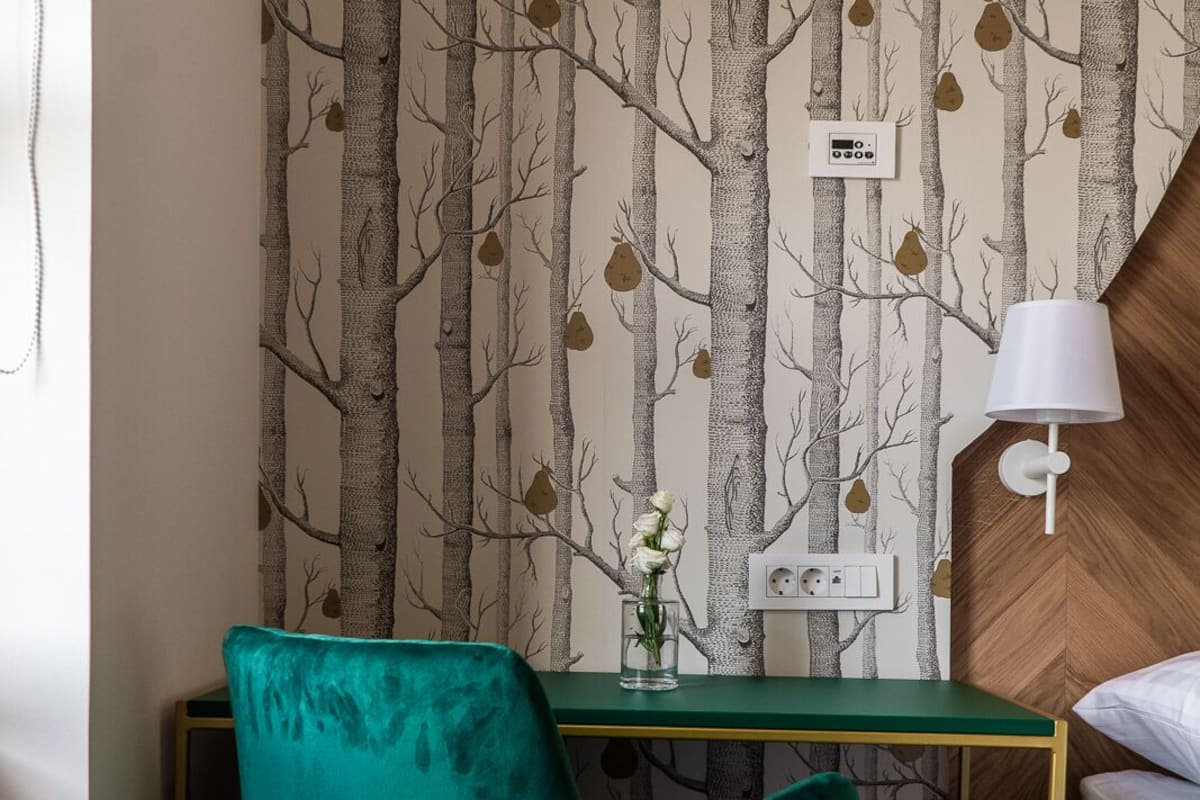 A room with a desk, a teal chair, a white lamp, and a wall with a tree pattern.