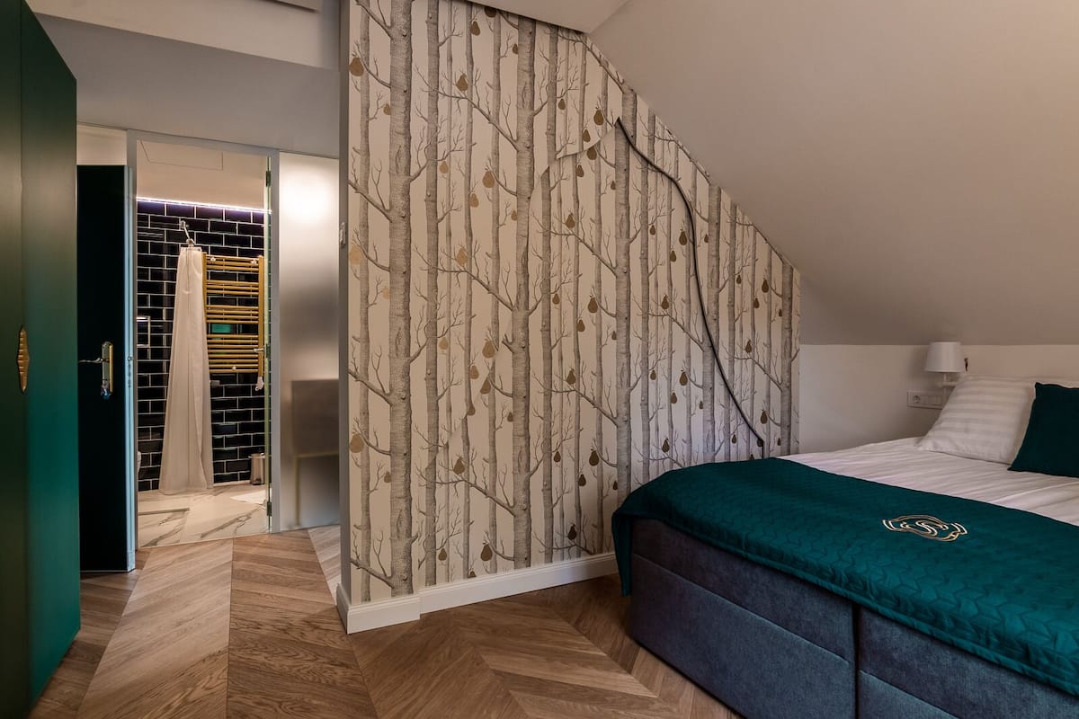 A bedroom with a bed, a nightstand, a wall with a tree pattern, and a door leading to a bathroom.
