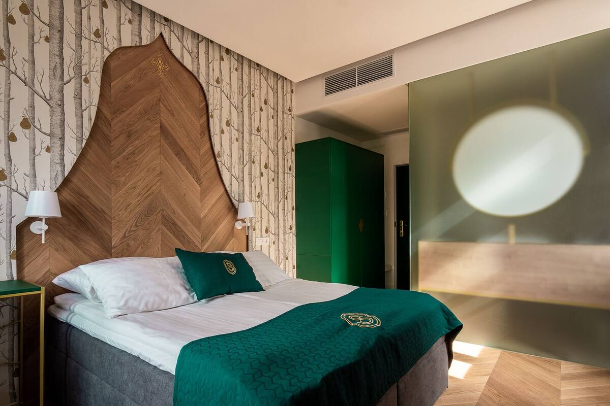 A modern bedroom with a wooden headboard, a green accent wall, and a large mirror.
