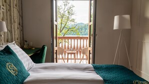 A bedroom with a bed, a chair, a table, and a view of a balcony with chairs and a table. - HOTEL STARKL HERITAGE & UNIQUE (Bled)