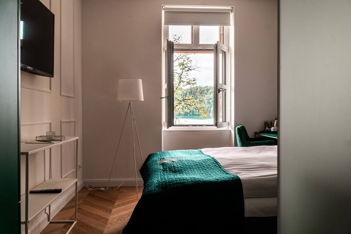 A bedroom with a bed, a desk, a chair, a floor lamp, and a TV on the wall.