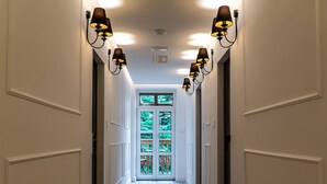 A hallway with patterned flooring, wall-mounted sconces, and a door leading to a green outdoor area. - HOTEL STARKL HERITAGE & UNIQUE (Bled)