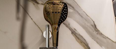 A showerhead with a gold finish and a modern design, mounted on a marble wall.