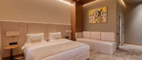 Una habitación de hotel moderna con una cama grande, un sofá, una mesita y un cuadro en la pared.