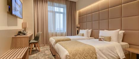 Habitación de hotel con dos camas, un escritorio con silla, televisión y un ventanal con cortinas.