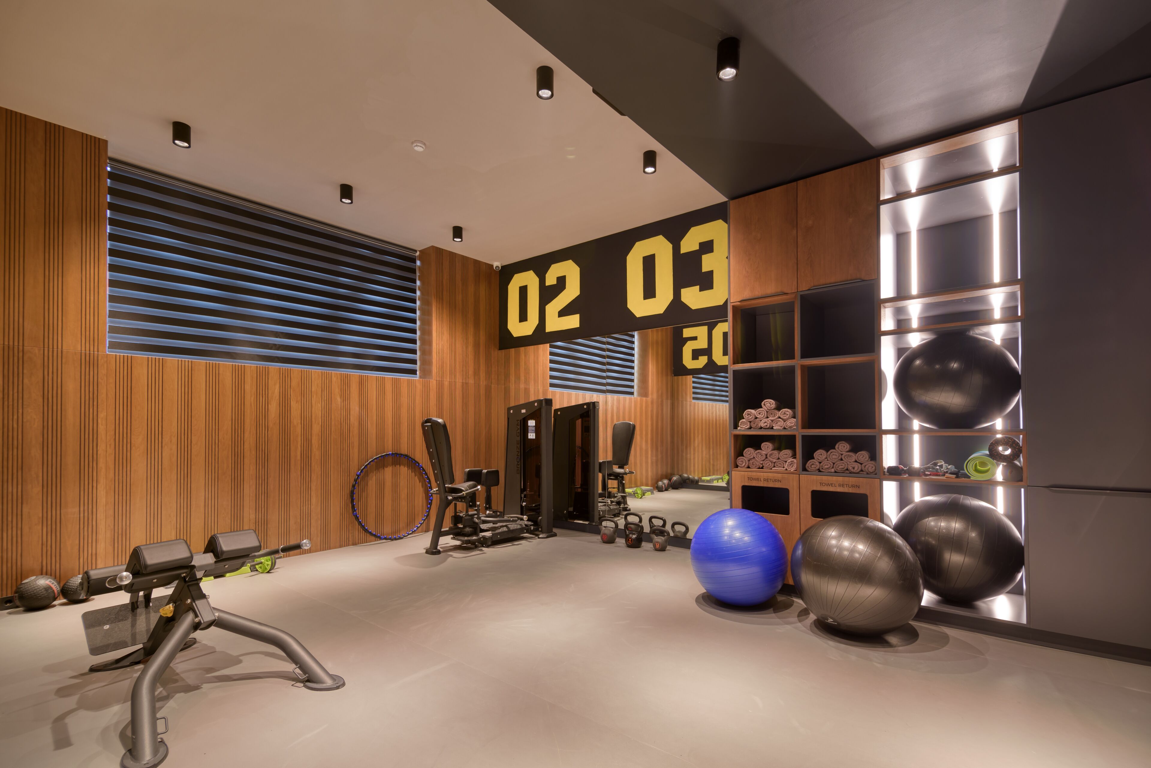 A modern gym with exercise equipment, a digital clock, and a wall with storage shelves.